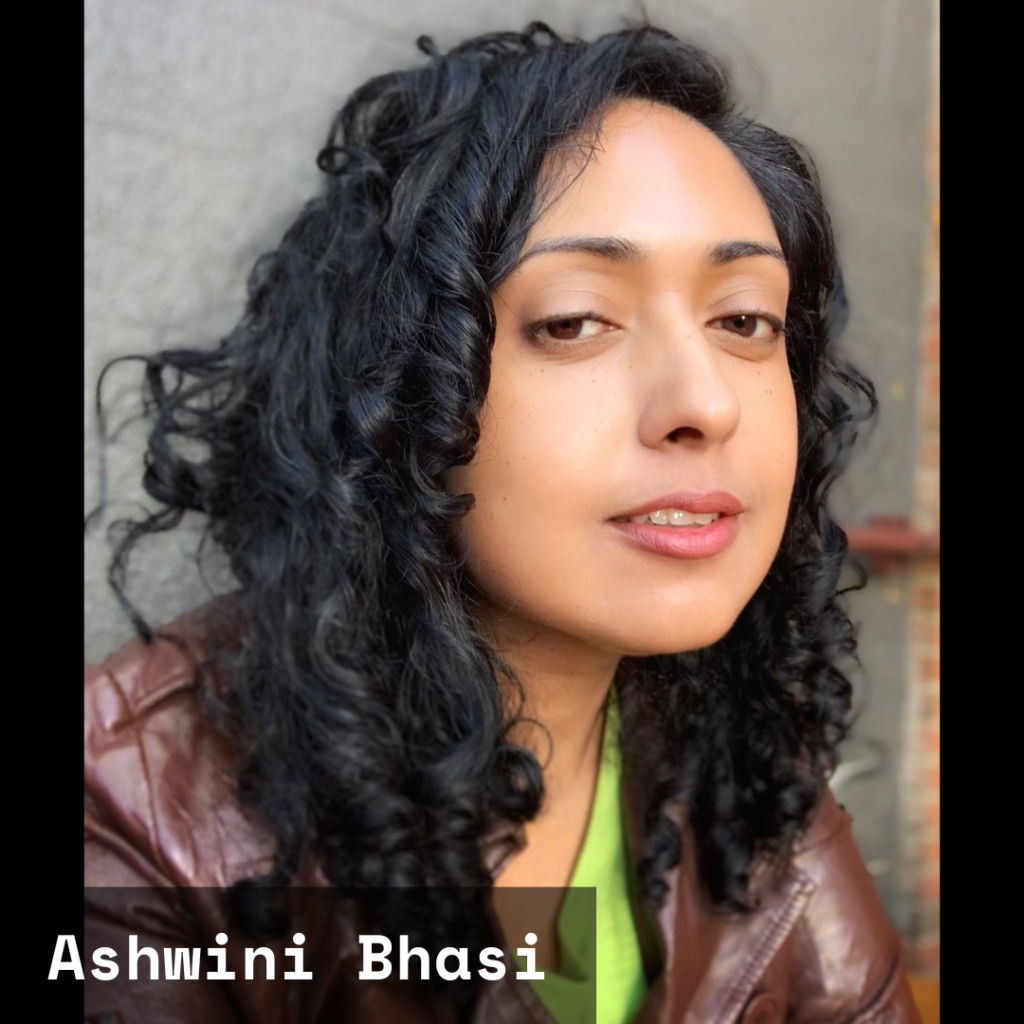 A photo of Ashwini Bhasi, an Indian female poet with long curly hair, wearing a brown jacket and a green shirt. 